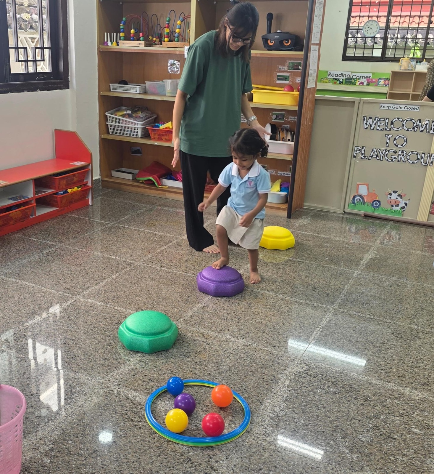 A Genius Gems teacher guiding a toddler across colourful stepping stones during a playgroup activity